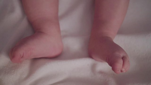 Tiny baby feet moving and curling toes on white blanket, Close Up