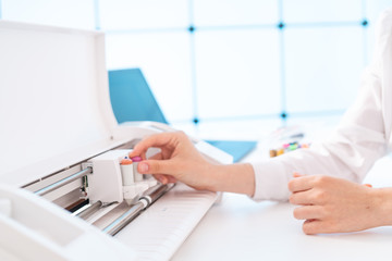 Young woman in printing office insert paper and color pens on plotter