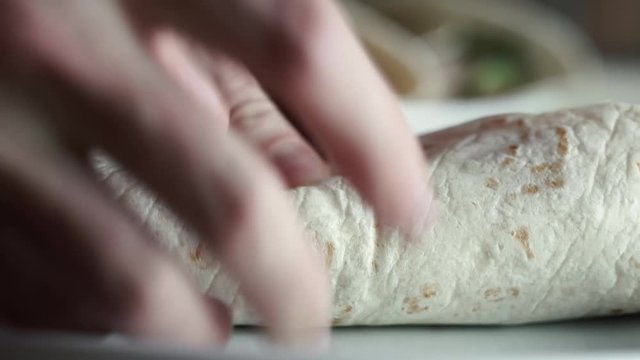 Male hands rolling tortilla bread around pulled pork meat with salad, avocado, and red bell peppers.