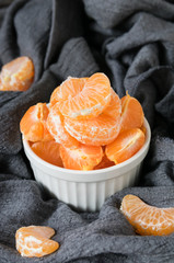 still life, slices of ripe mandarin in a white plate on a background of gray draped fabric