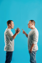 Vertical shot of young adult Caucasian man scolding his twin brother for something, bright blue...