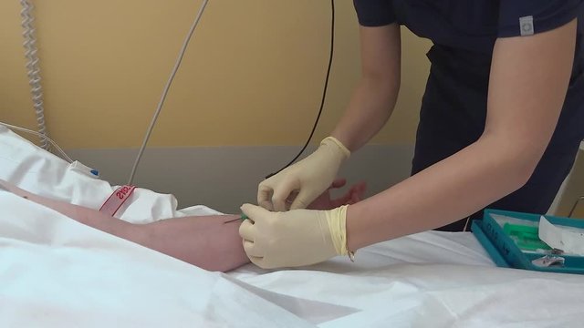 The technology of connecting the drip to a venous catheter. An unidentified masked nurse connects the infusion system to a venous catheter and checks how the medicine enters the vein.