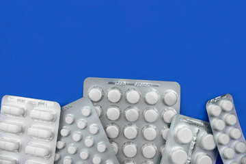 White new medicine pills in blister packs close-up flat lay on trendy blue background. Top view with copy space. Disease, illness, virus concept. Pharmaceutical blister pack antibiotics. Stock photo.
