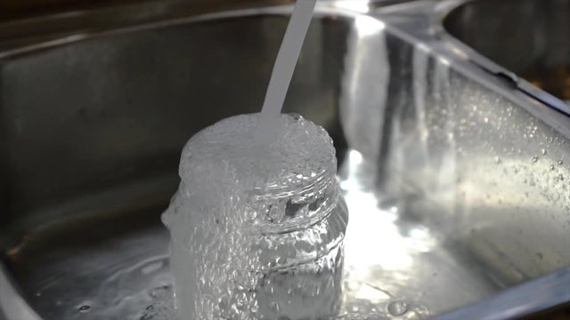 Tap water flowing into container and overflow to the sink. Slow motion.