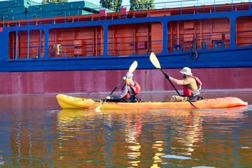 Couple paddle kayak near a big ship on the Danube river
