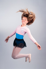 Full length portrait of carefree young 11 year old girl in dance outfit jumping legs bent isolated...
