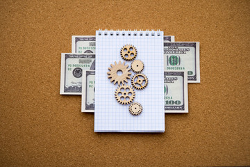 Obraz premium Wooden gears, Notepad, American dollar bills on the background of the cork Board. Business, financial planning.