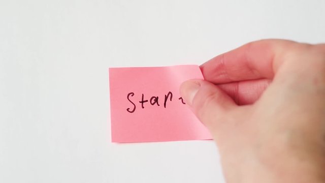 Hand sticks a sticker on a white background with the handwritten text "Start".