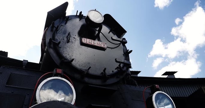 Historic steam locomotive with license plate and lights on sunny day and clouds passing by, Time Lapse