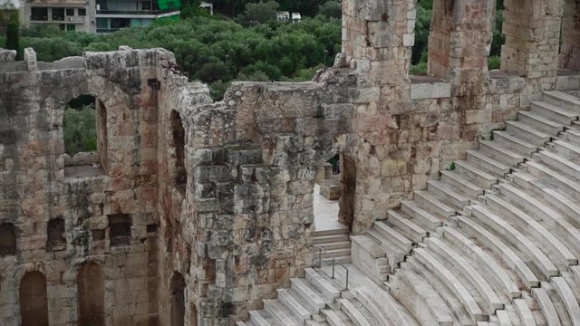 Rising view of the steps and seats of the ancient Roman theater Odeon of Herodes Atticus on Filopappou Hill in Greece, showing trees and Athens buildings in the background
