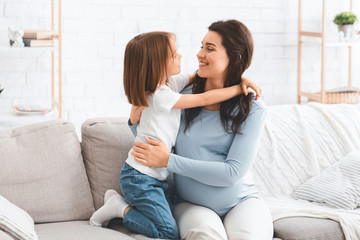 Little kid hugging pregnant mom, home interior