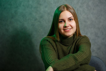 Obraz premium Girl in a green sweater and jeans on a gray chair and smiling