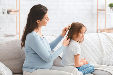Loving pregnant woman combing her little daughter hair