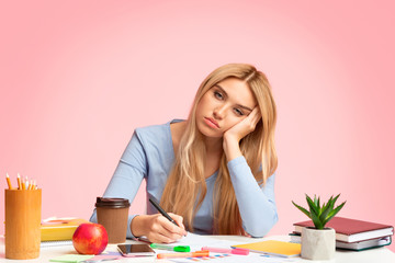 Tired teenage girl sitting at desk writing