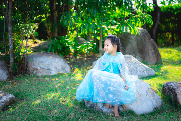 Portrait of cute smiling little girl in princess costume sitting on the rock in the park