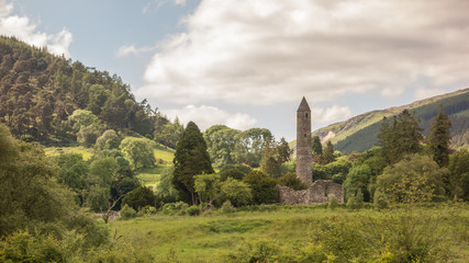 Fototapeta na wymiar The Round Tower and woodland at Glendalough, Co. Wicklow, Ireland. The Glendalough valley is located in Wicklow Mountains National Park and is home to an Early Medieval monastic settlement.