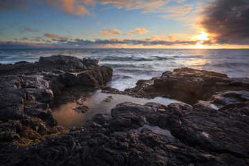 A rocky shore of solidified lava during sunset.
