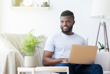 Positive black man typing on laptop at home