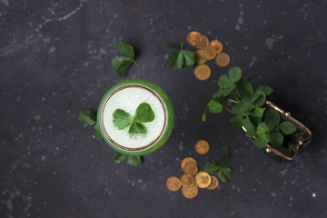 Fresh clover leaves from a green purse and gold coins are scattered on a dark background. St....