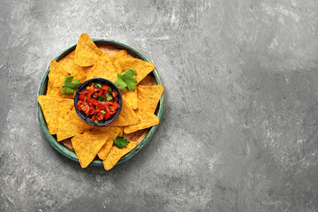 Salsa sauce and nachos on a plate, gray concrete stone background. Traditional latin american appetizer. Top view, flat lay.