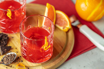 Two glasses of chocolate red orange negroni, alcoholic bitter cocktail served by ingredients on the light gray table.