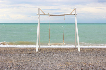 Empty wooden swing on the beach. Empty beach, blue sky.