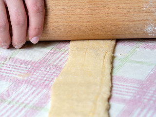 the Baker rolls the dough into strips on the kitchen table, sprinkled with flour.