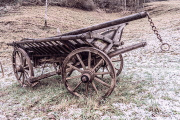 Fototapeta na wymiar alter Leiterwagen, Holzwagen auf einer Alm im Winter auf von Reif bedeckter Wiese am Waldrand, style: sepia, old