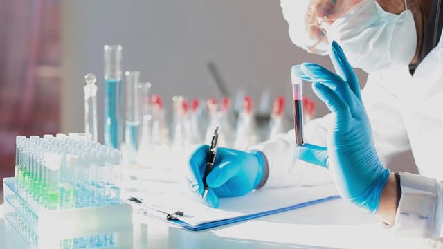 Researcher in a laboratory holding a tes tube with blood sample and make a notes.