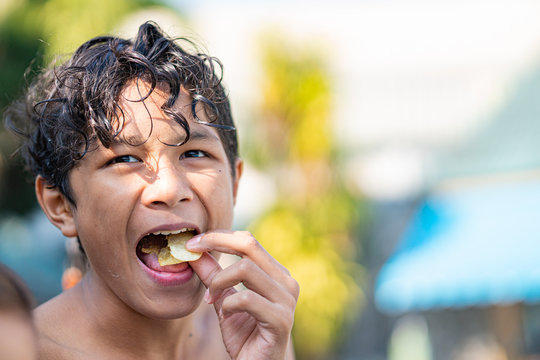 young Asian boy eating snack food with mouth open wide