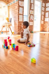 Beautiful african american toddler playing with wooden blocks train toy around lots of toys at kindergarten