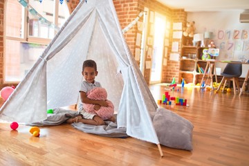 Beautiful african american toddler playing inside tipi smiling at kindergarten