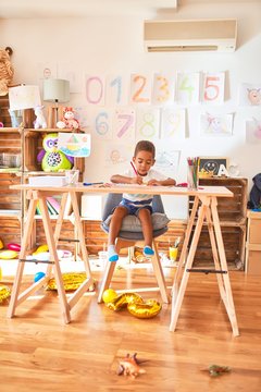 Beautiful african american toddler sitting drawing using paper and pencils on desk at kindergarten