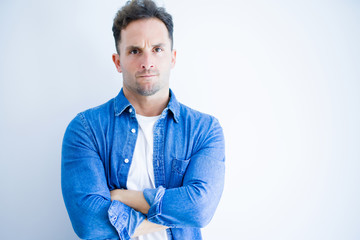 Young handsome man wearing denim shirt standing over isolated white background skeptic and nervous, disapproving expression on face with crossed arms. Negative person.
