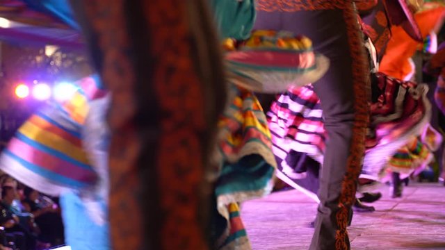 Camera pans left showing the beautiful chaos of Mexican dancers with flowing dresses.