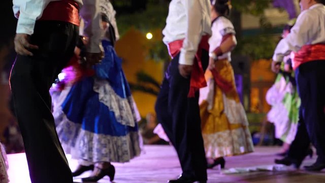 The backs of Mexican folk dancers as they perform on a stage.
