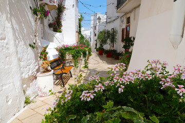 Scenic sight of the Ostuni town sunny street with bench and blooming flowers, Apulia region, Italy, Adriatic Sea