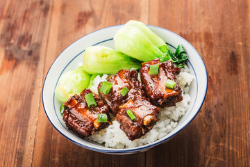 A bowl of rice with ribs in brown sauce