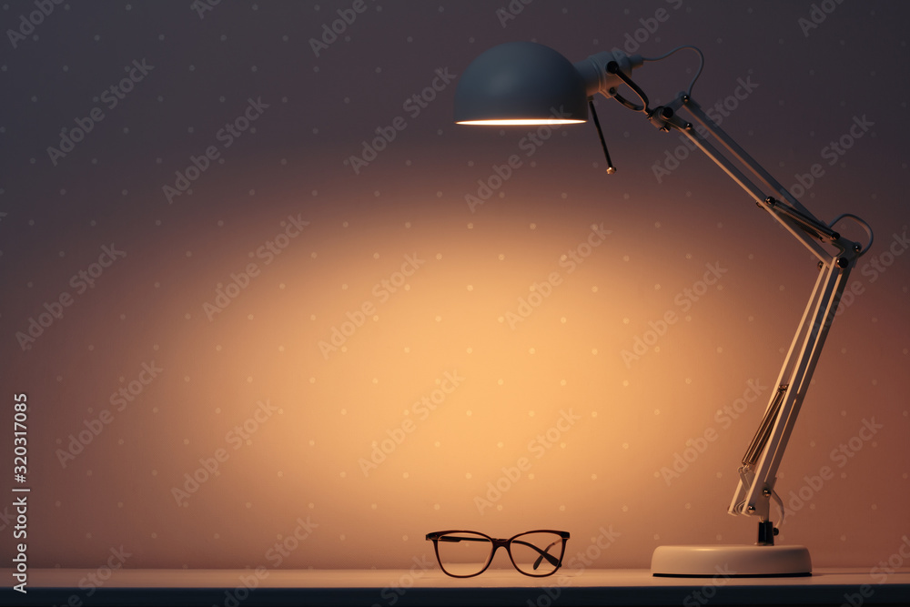 Wall mural work lamp in the dark with the light on, shining on the glasses on the table