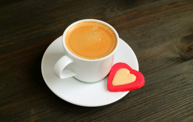 Cup of hot coffee with a heart shaped butter cookie on dark brown wooden table