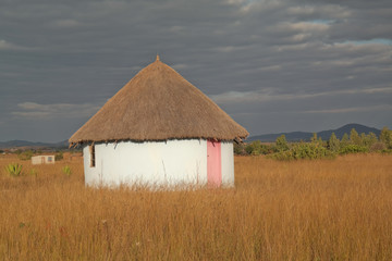 A traditional African thatched hut, dwelling in a village, yellow grass and dark cloudy sky, in Mashonaland, Zimbabwe, Africa.