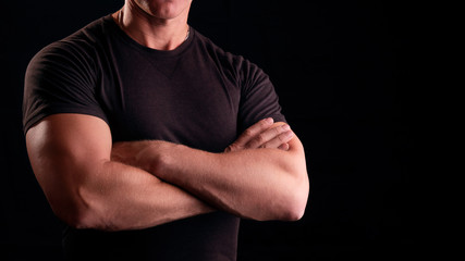 A man with strong arms. Male security guard in a black t-shirt. Strong man on a black background....