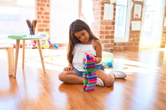 Adorable toddler sitting on the floor. Playing with wooden building blocks at kindergarten