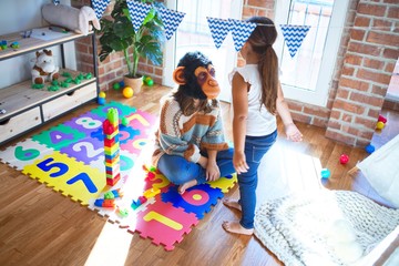 Beautiful teacher and toddler playing with monkey mask around lots of toys at kindergarten