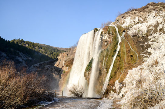 Waterfall with rainbow at sunset at cold winter day. Falling water of Krcic into the source of the Krka River. 22 meter high waterfall. Topoljski slap, Krka, Knin, Croatia. Ice and snow.  
