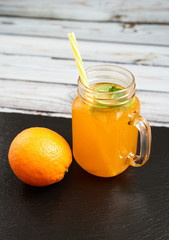 Fresh orange with oranges on a slate board on a light wooden background. Summer refreshing drink..Fresh orange in a glass jar with mint and oranges.