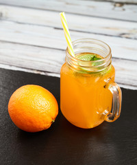 Fresh orange with oranges on a slate board on a light wooden background. Summer refreshing drink..Fresh orange in a glass jar with mint and oranges.