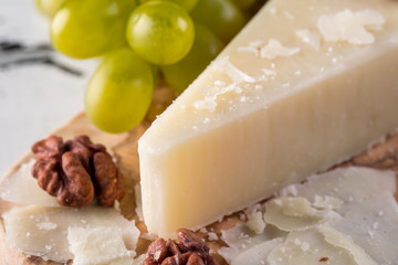 Pecorino romano, hard italian sheep milk cheese on wooden cutting board with grape, selective focus
