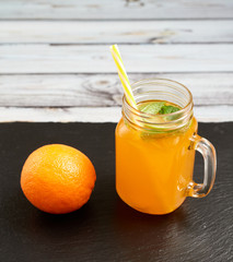Fresh orange with oranges on a slate board on a light wooden background. Summer refreshing drink..Fresh orange in a glass jar with mint and oranges.
