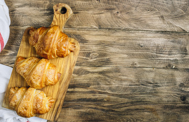 Croissant on wooden cutting board on rustic wooden table. French breakfast. Top view. Flat lay. Copy space.